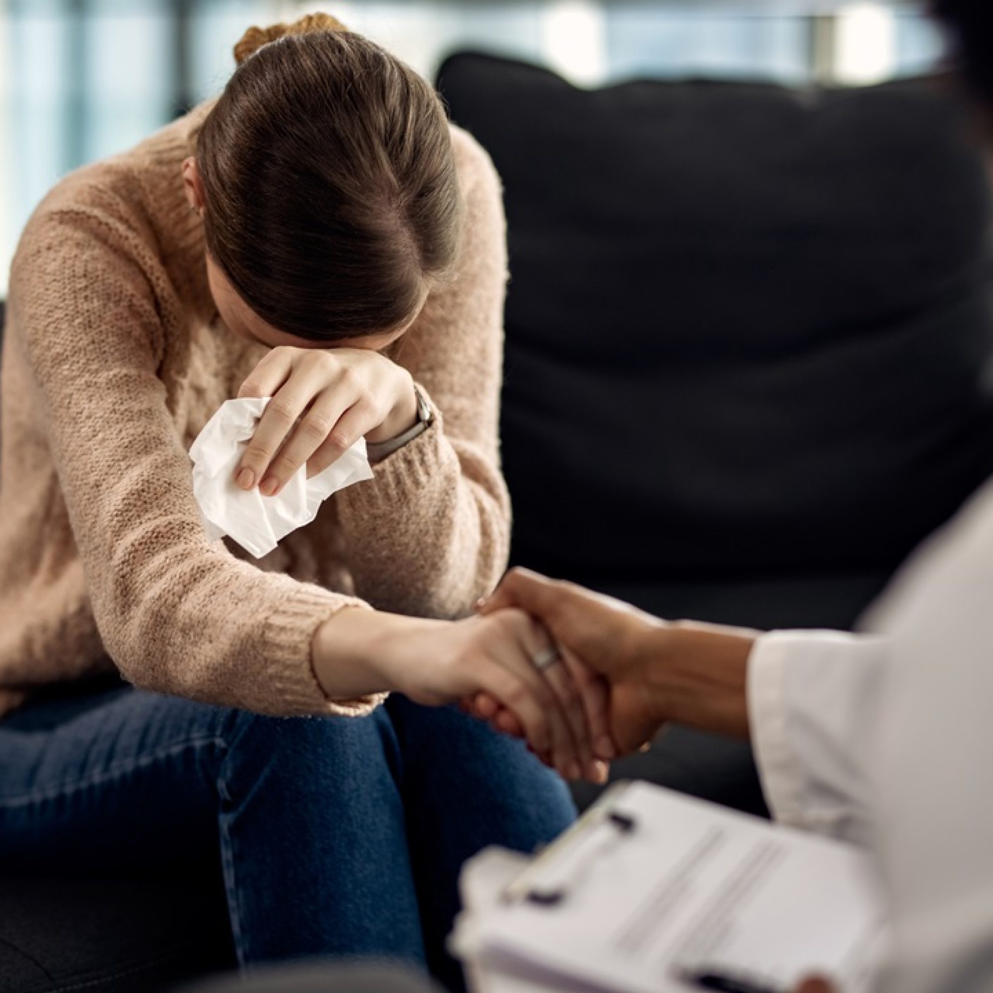 Sad woman crying while holding hands with her psychotherapist at doctor's office.